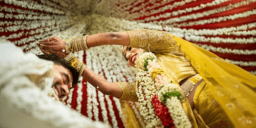 Bride in yellow lehenga during traditional Indian wedding ceremony, lying under vibrant floral canopy with festive vibes.