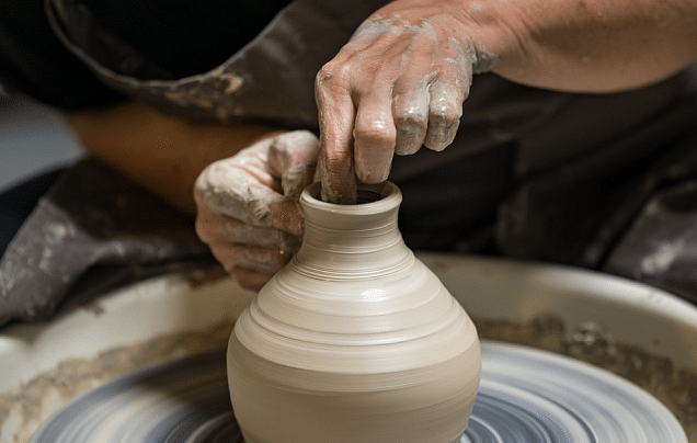 Potter shaping clay vase on a wheel, hands covered in clay, close-up shot.