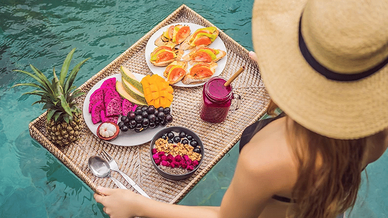 A woman in a sun hat relaxing by the poolside with a platter of fresh fruit - S Hotel Montego Bay, Jamaica