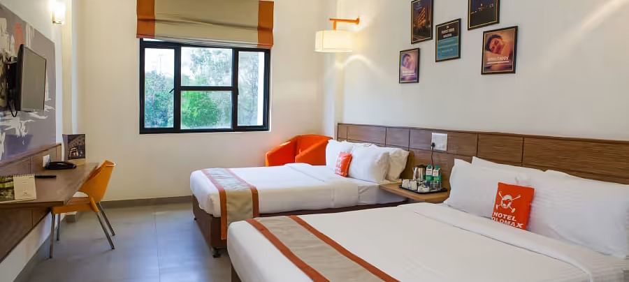 View of a hotel room featuring two comfortable beds, wall art, and a large window with natural light - Max Hotel Prayagraj.