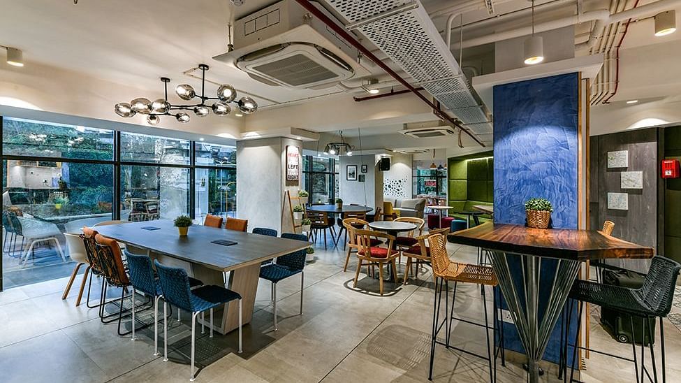  A spacious working area with numerous chairs and tables arranged, complemented by warm lighting at Indie Stays