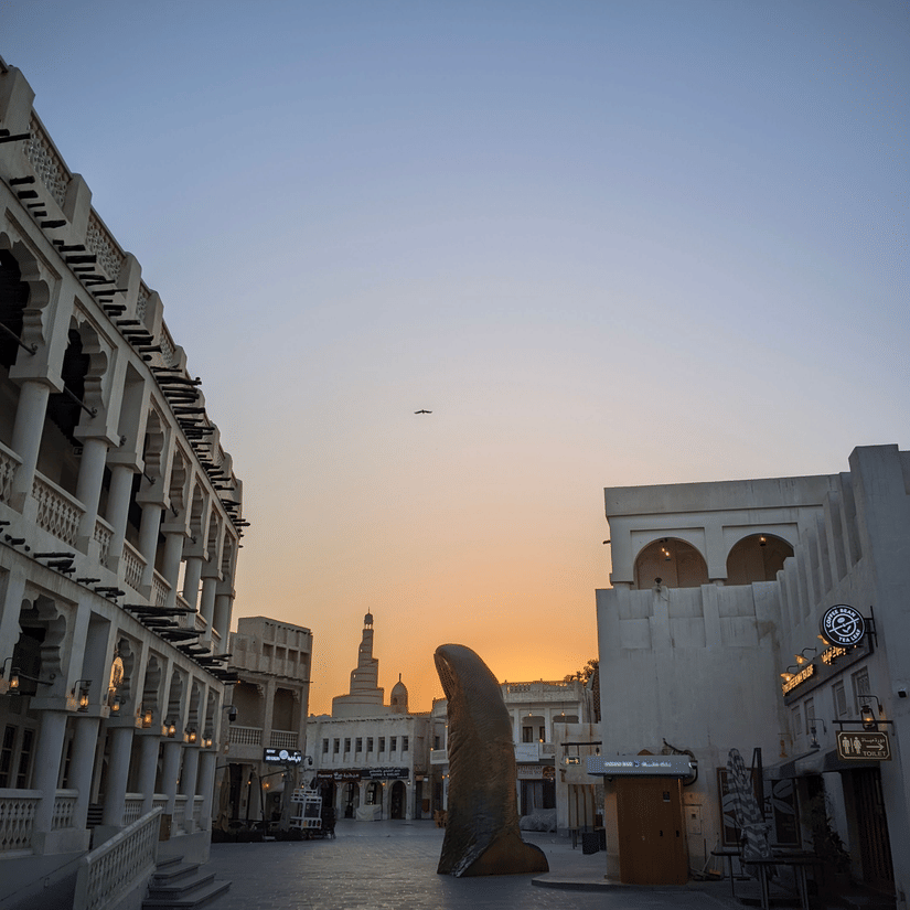 A view of a street in Souq Waqif in Doha during twilight hour with a new gold thumb statue in the centre.