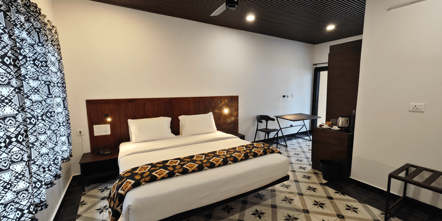Modern guest room interior with a king size bed, decorative floor tiles, and dark wood ceiling accents - Ibex Resorts, Malampuzha (Kava Eco Camp and Caravan Park)