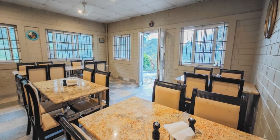 Seating arrangements inside a restaurant with a brown golden table and chairs - Ibex Stays & Trails, the best resort in Valparai.