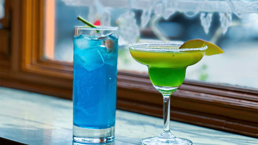 A blue beverage and a green cocktail glass sit on a ledge next to a window at Amantra Shilpi Resort, Udaipur.