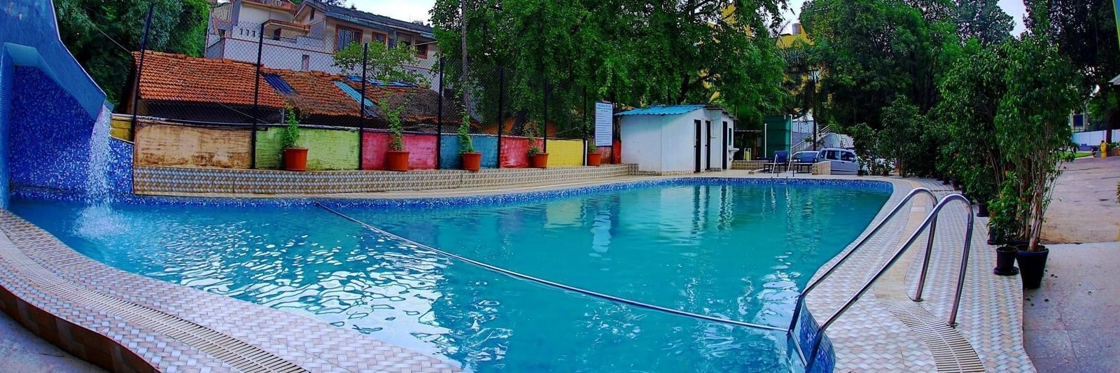 Assymetrical large swimming pool at Krushnai Resort under a partly cloudy blue sky.