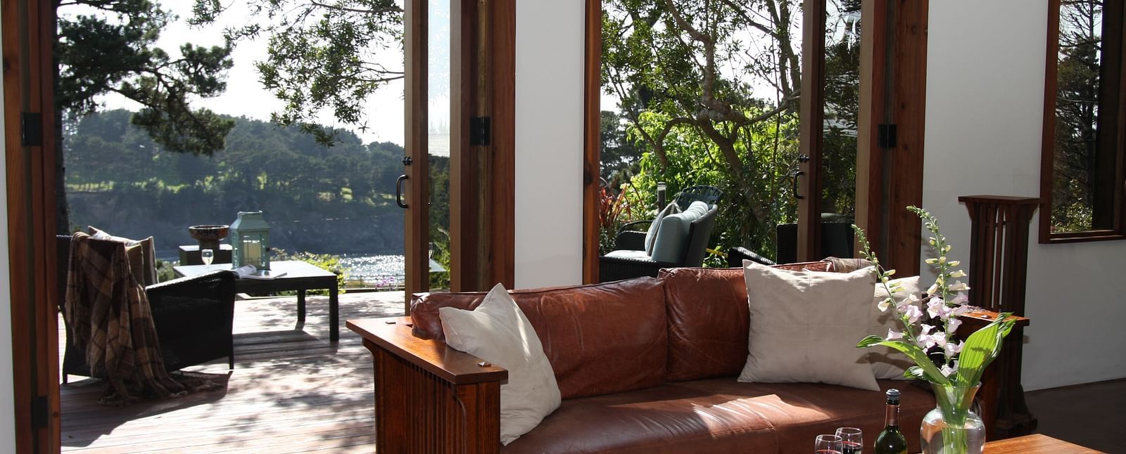 A cozy leather couch and a table with a flower vase illuminated by sun rays entering through the large windows of the room - Brewery Gulch Inn & Spa