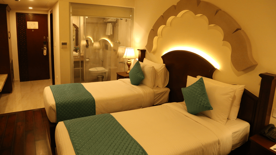 A bedroom at Comfort Inn Sapphire by Eastlynn Collections, Jaipur with 2 single beds, side tables, headboard design, lamps, and wooden flooring.