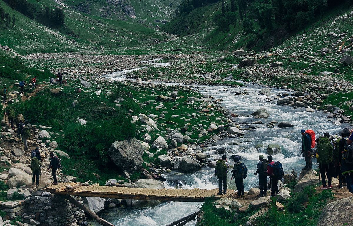 an image of people crossing a stream with the help of a small bridge