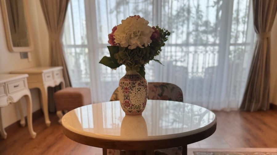 Cosy seating area with floral armchairs and a round wooden table beside sheer drapes - Mayfair Cafe & Suites, Dalhousie