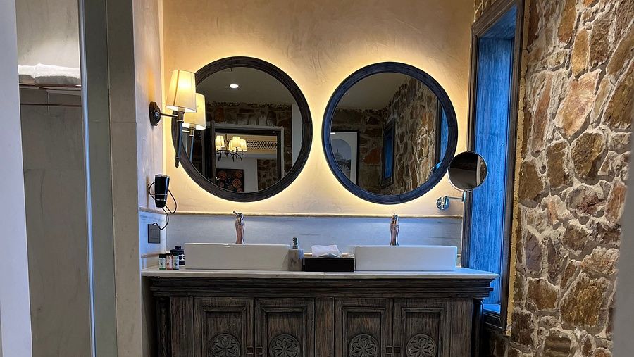 A dressing area with two mirrors on the wall, a cabinet below, and an LED strip around the mirrors, creating a warm lighting ambience