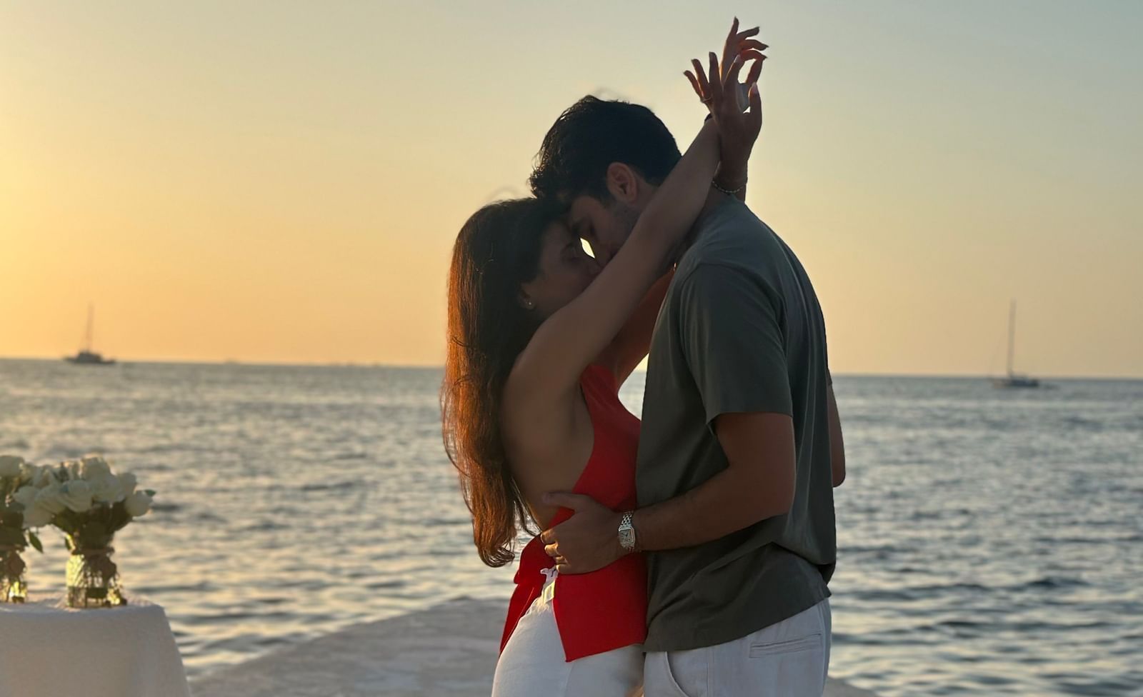 A silhouette of a couple kissing on the pier with floral decorations scattered as the sun sets over the water at Casa Morada.