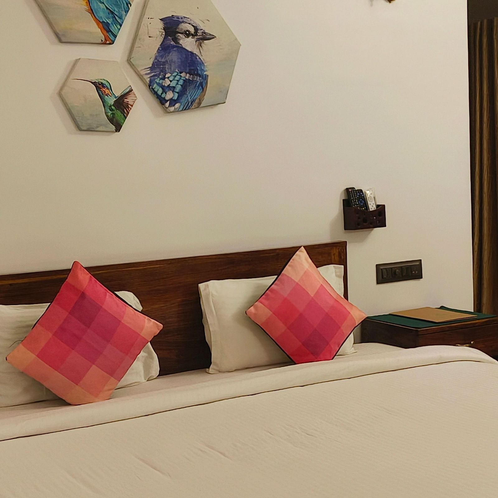 Front view of a double bed with two pink pillows kept on it and hexagonal frames hanging on the wall in 101 non-ac room at Ananda Holiday Home, Wayanad 1