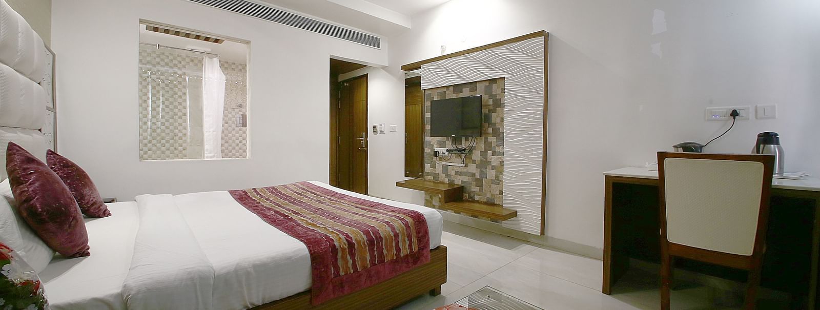 Elegant room with a large bed, table, chair, and TV unit at Hotel Emerald, Chandigarh