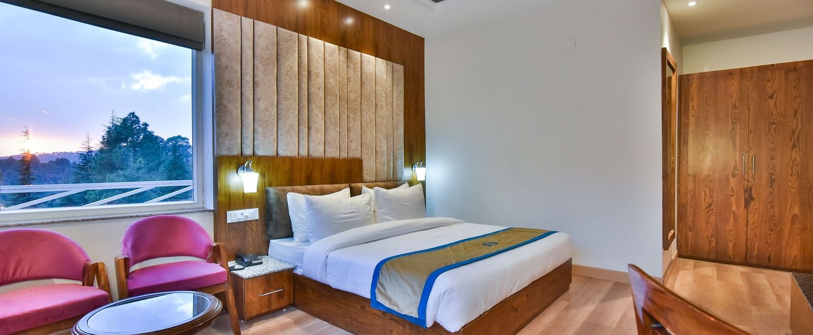 A large bed next to two cushioned chairs  in Premium Room With Balcony at DLS Ark Holiday Inn, Banikhet.