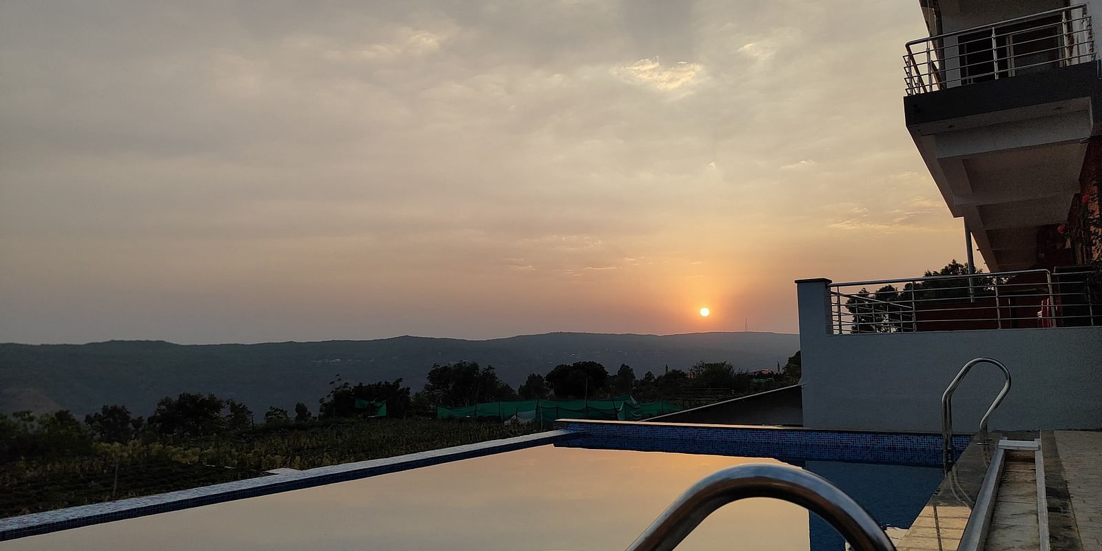 A view of the swimming pool overlooking the sunset surrounded by hills.