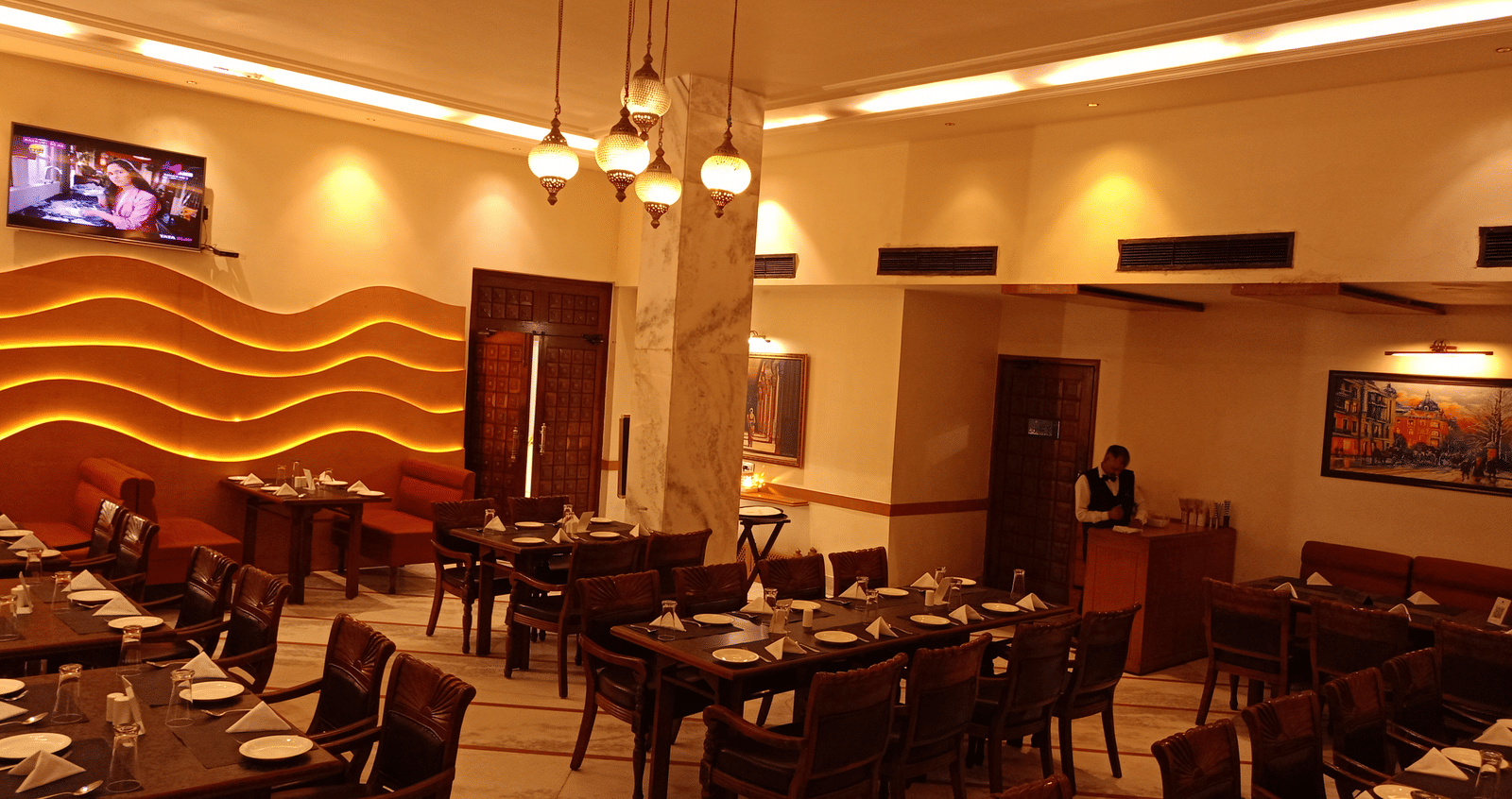 Dining area at Hotel Gold, Panipat featuring set tables, chairs, and a wavy patterned wall design.