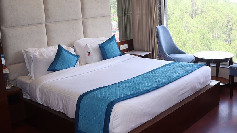Side view of Deluxe room with plush bed and bedside tables, seating area with coffee table - Mastiff Hotel, Dalhousie