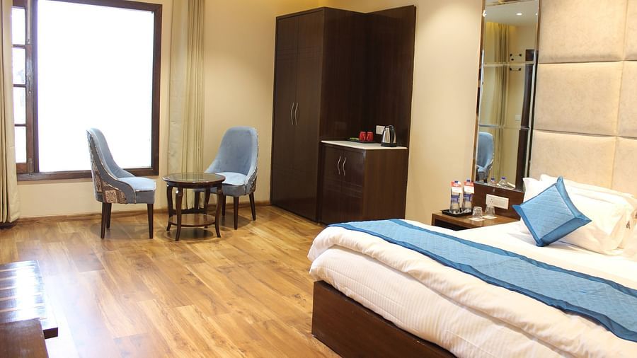 Side angle view of the Superior room with plush bed with bedside tables scenic view from the window with curtains and seating area - Mastiff  Hotel, Dalhousie