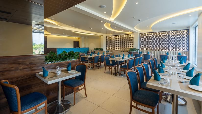 Modern restaurant at Mastiff Grand The Sia Palace Suites & Banquets, Khopoli, featuring well-lit dining tables, jali patterned walls, and a contemporary design.