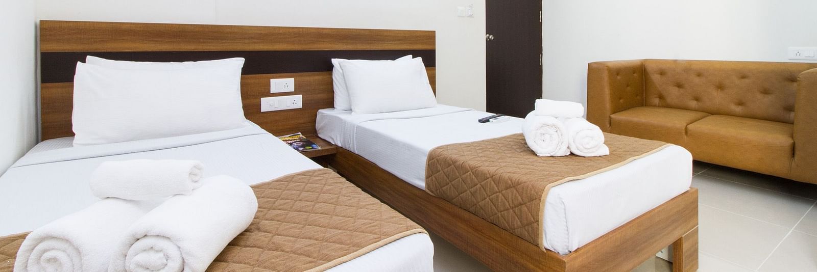 A room at Sanctum Suites Whitefield, Bangalore including twin beds with brown and white bedding and a sofa.