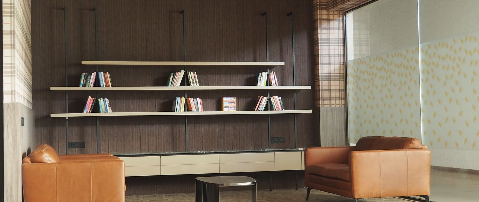 A lounge area with armchairs and shelves, separated by a glass partition - Club Charholi, Pune 