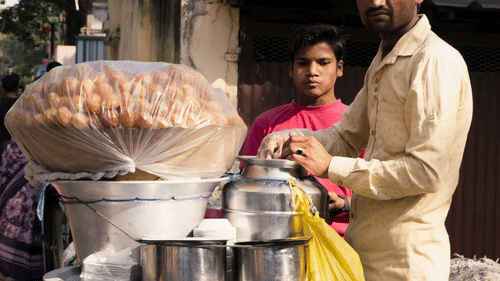 a person making pani puri from a pani puri stall while a person looking from behind