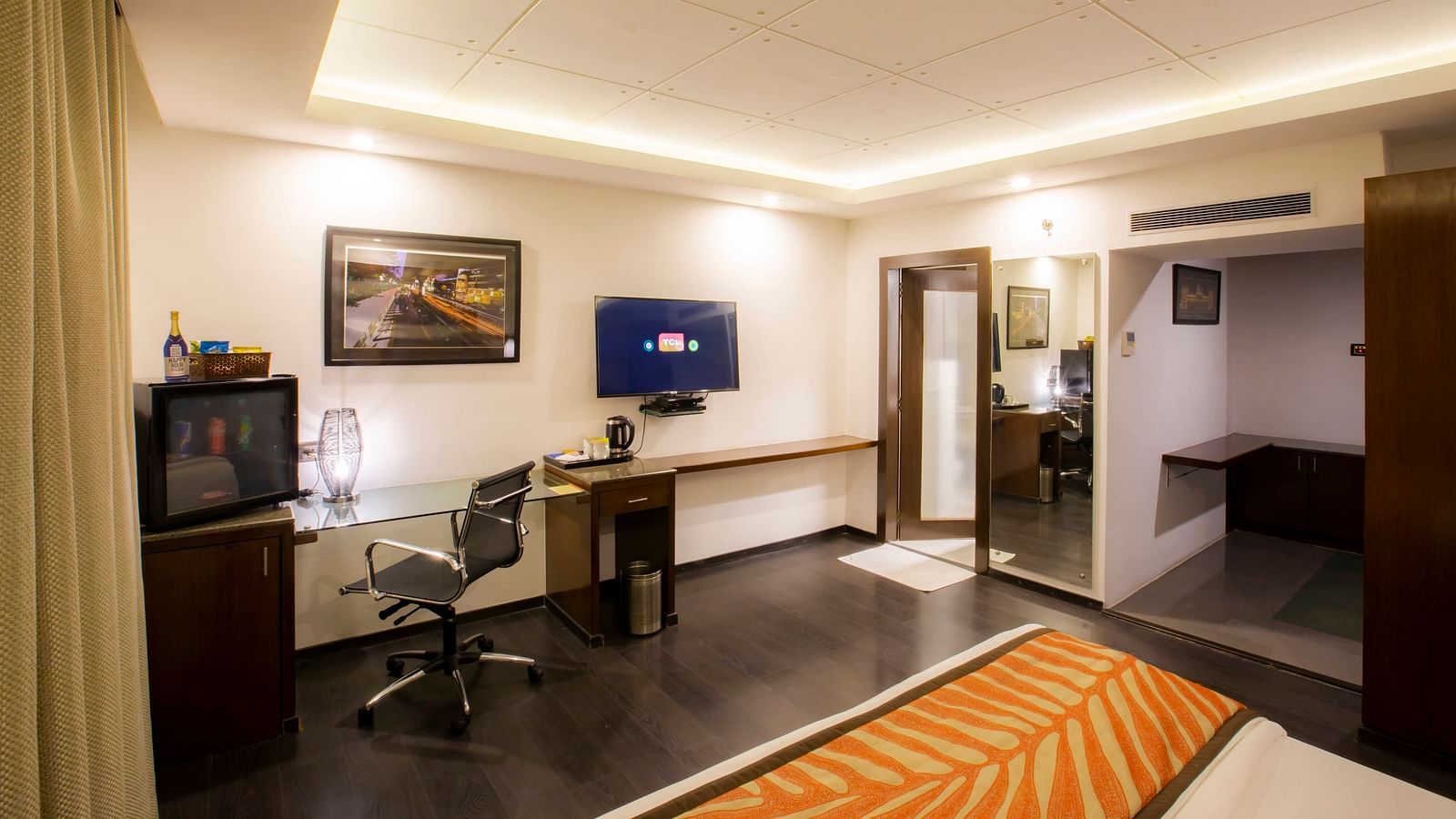 A well-lit Studio Room at The Cunningham Hotel featuring the bed facing the TV mounted on the wall beside which is a work desk by the window