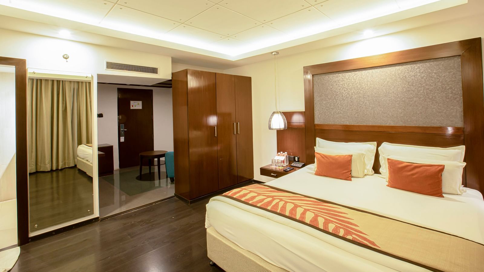 Studio Room at The Cunningham Hotel with warm lighting, a plush bed with a large headboard and a mirror attached to wall next to the wardrobe