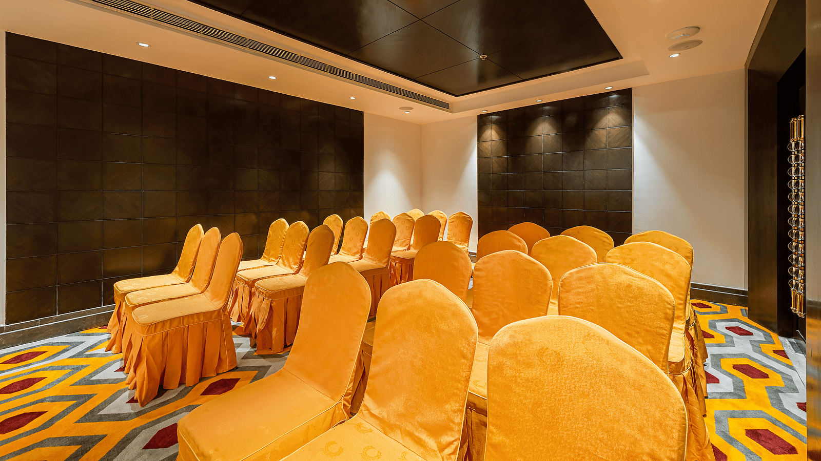 Conference room with yellow-orange chair covers, a dark tiled wall and a patterned carpet - TGI Grand Fortuna, Hosur