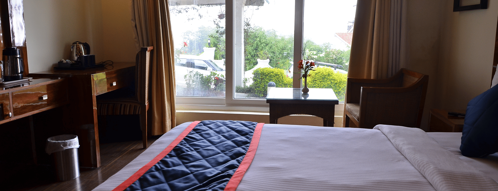 A room with a comfy bed, desk area, and balcony offering views of lush greenery - Benzz Park, Kodaikanal