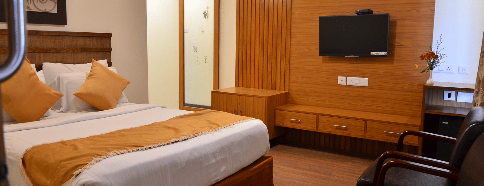 An elegant room with a queen bed, wooden furnishing, and a wall-mounted TV for a relaxing stay - Benzz Park, Kodaikanal