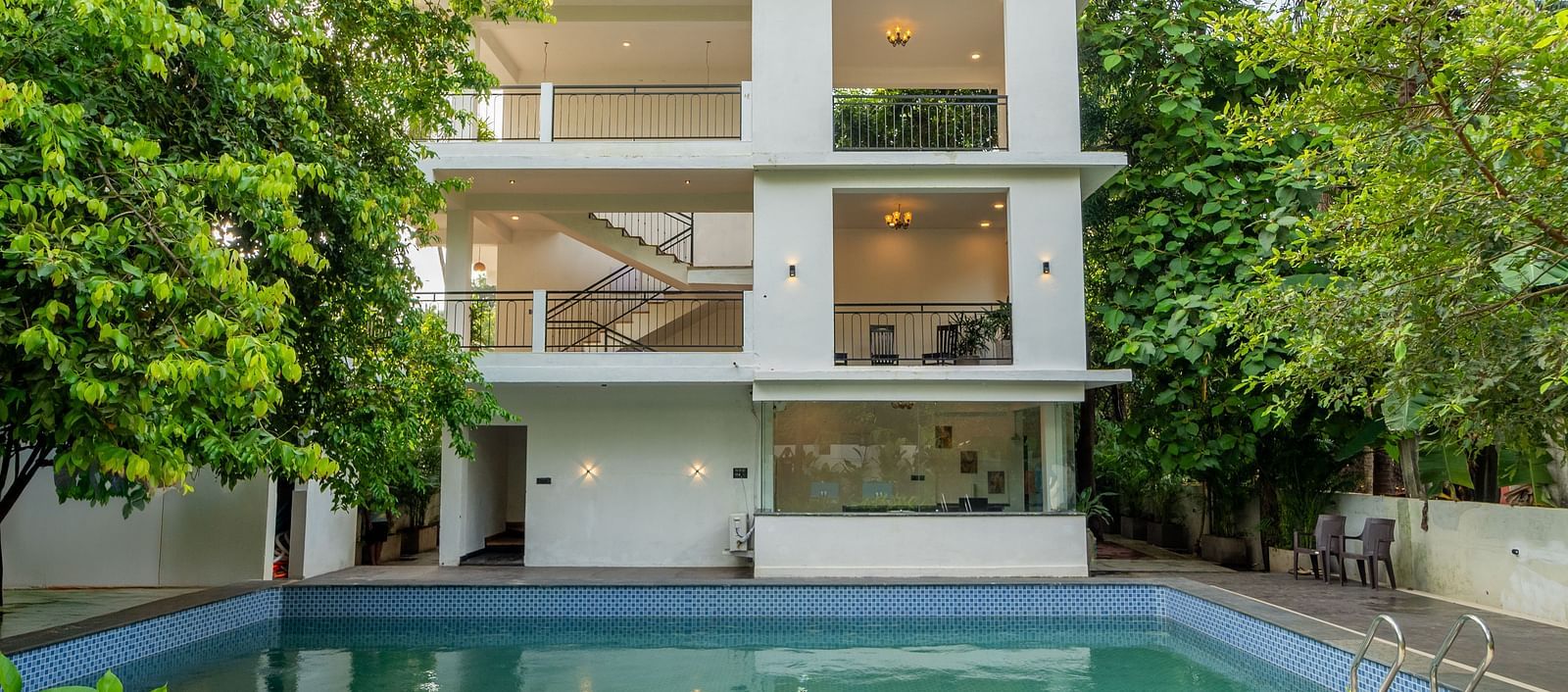 Modern white building with a swimming pool surrounded by greenery at De Soul Santé Hotels & Resorts.
