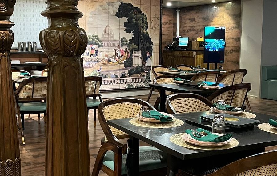 Elegant restaurant interior featuring set tables with place settings, ornate columns, and a large mural on the back wall - Astra Hotels & Suites, Spice Garden Layout