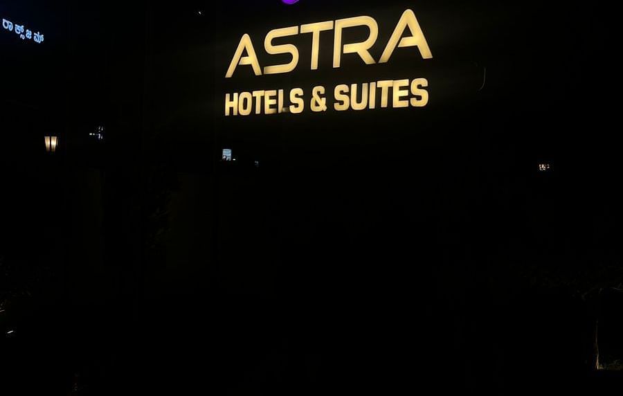 Brightly lit Astra sign in purple and yellow against a dark night background, with smaller text hotel & suites below.