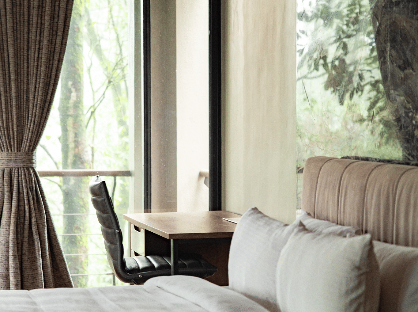 A close-up of a bed at Stanley Revelation with white sheets, and a desk and chair visible in the background.