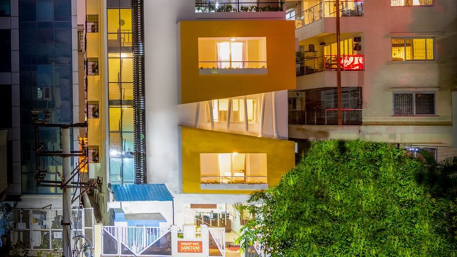 A facade of Sanctum Suites Domlur, Bangalore with brightly lit windows against the night sky.