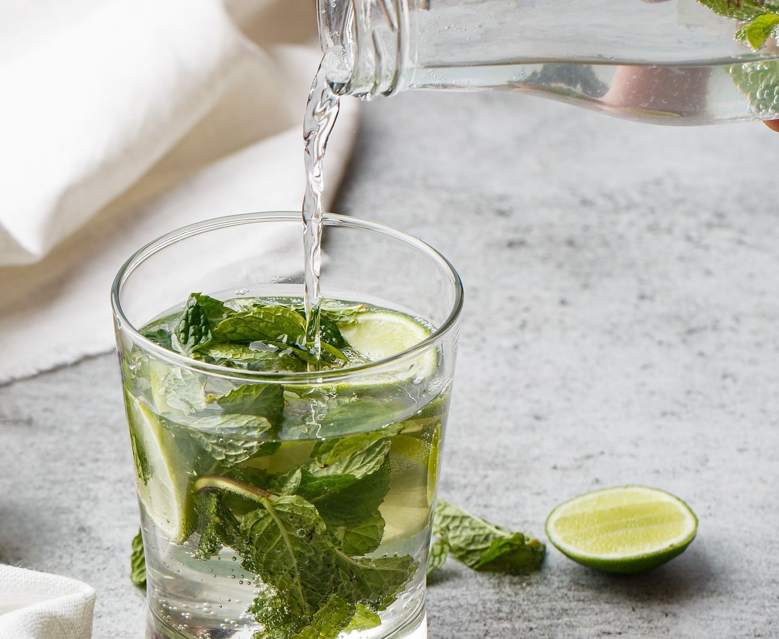 Water being poured into a glass filled with fresh mint and lime slices, creating a refreshing beverage.
