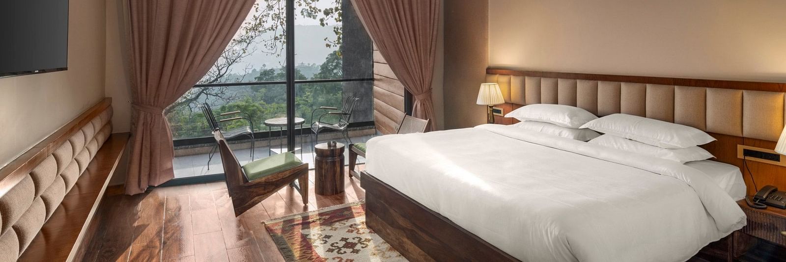 A cosy bedroom with a wooden floor and ceiling, large draped window with a scenic view, and a comfortable sitting area - The Samai, Bhimtal