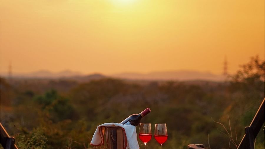 two chairs with a small table that has two glasses and a bottle of bubbly on it and sun setting in the background - Chunda Shikar Oudi, udaipur