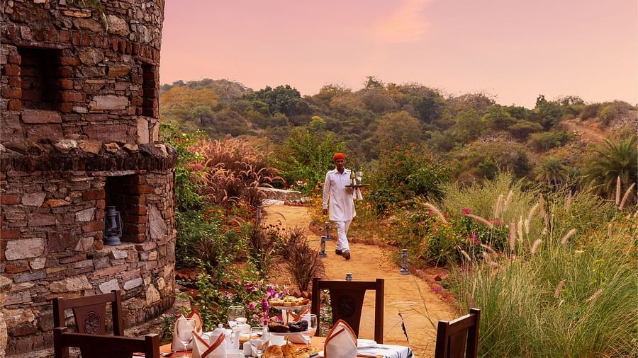 a table for four set up next to a stone building with greenery surrounding it - Chunda Shikar Oudi