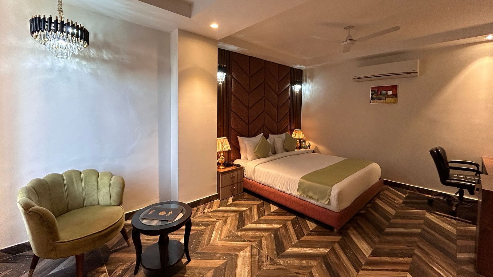 Image of Super Deluxe Room at DLS Grand Luxotica, Dehradun featuring a sitting space including a couch and a coffee table placed at a distance from the plush bed under warm lighting