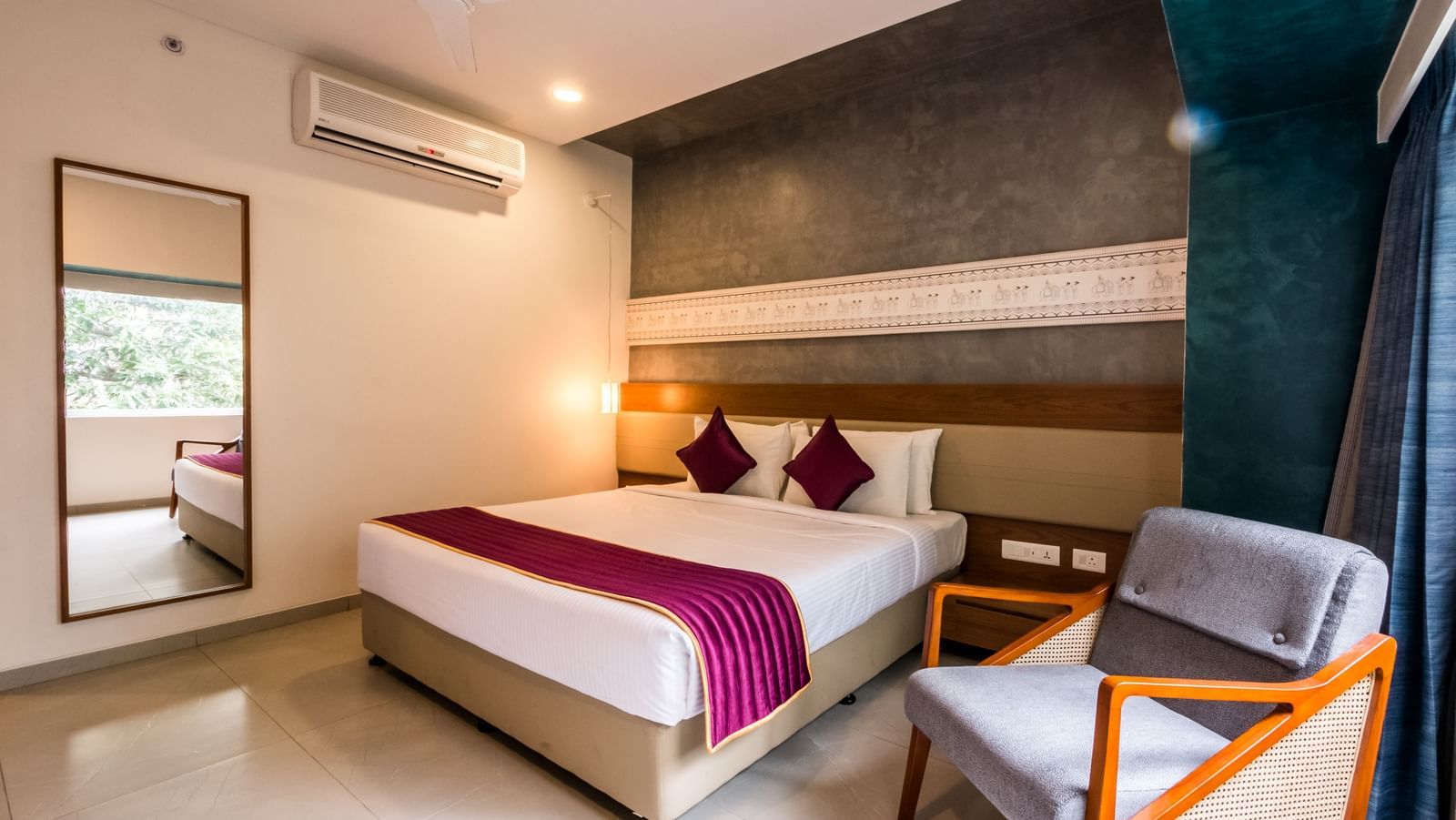 A spacious hotel room featuring a large bed, a full length mirror, and a comfortable armchair at Shilton Dee Cee.