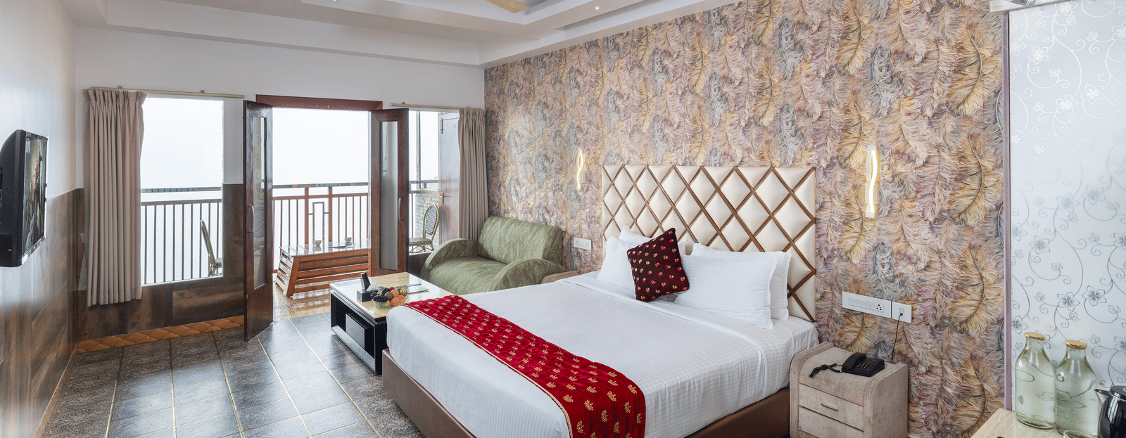 The interior of the Premium Club Suite at Parakkat Nature Hotel and Resorts, Munnar, featuring a large bed, a stone-patterned accent wall, a seating area, and sliding doors to the balcony.