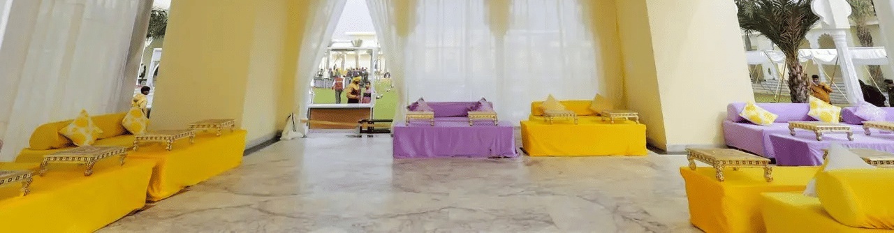 Indoor hall with ceiling decor, long seating arrangement, and tables at Beelwa Palace, Jaipur