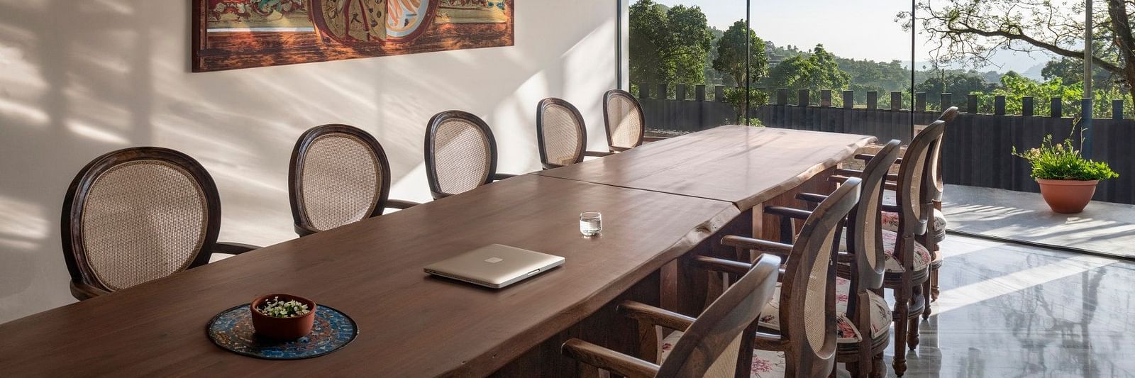 A meeting room with a long table in front of a glass door opening to a lush green garden - The Samai, Bhimtal