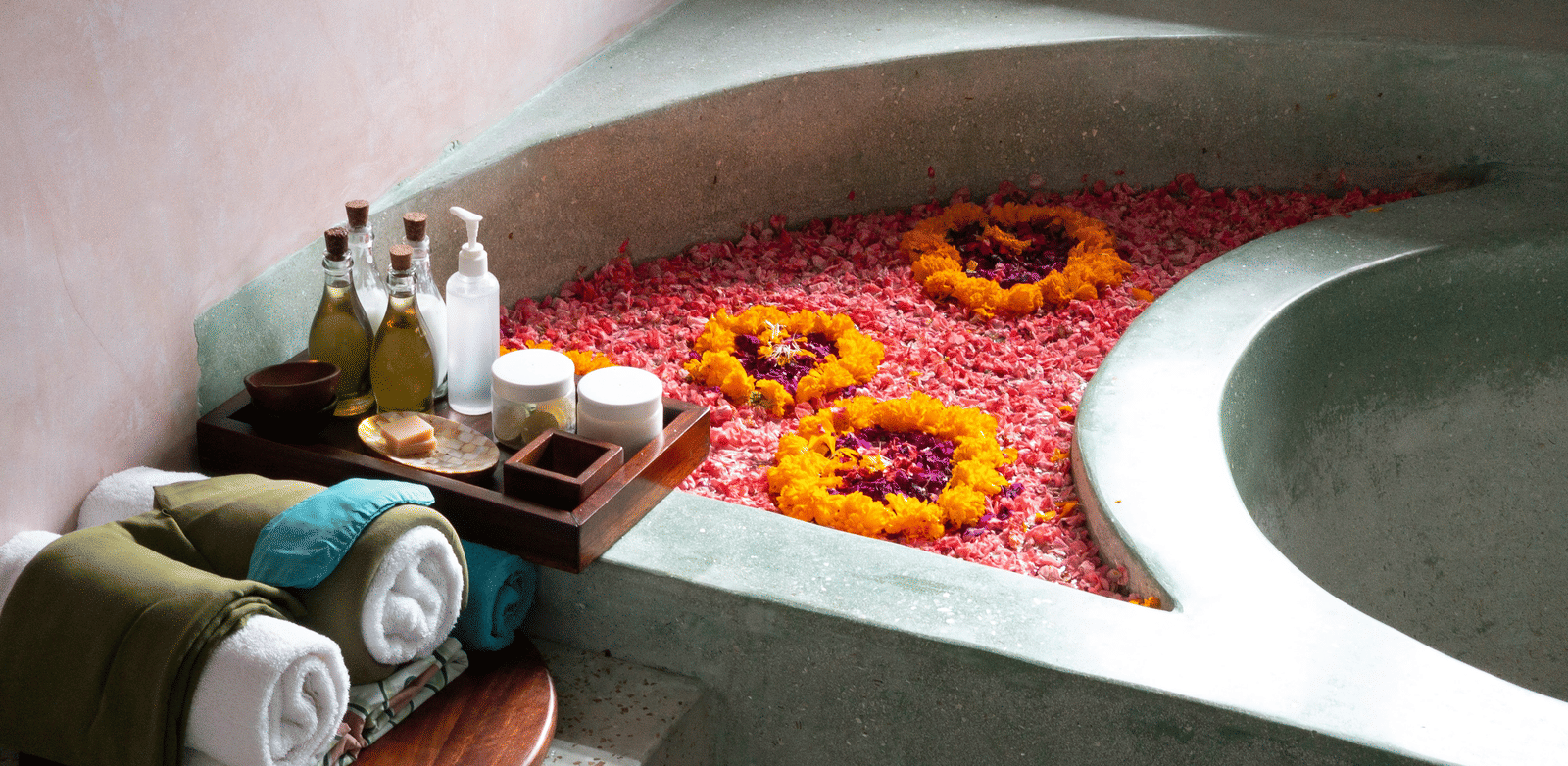 A stone bath filled with water and vibrant flower petals, surrounded by spa amenities.
