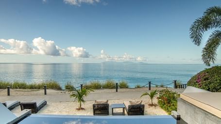 Tranquil beachfront view from a private infinity pool and terrace, overlooking calm Caribbean waters and a clear blue sky.