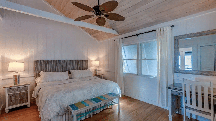 Bright bedroom with a double bed, ceiling fan, white walls, and a baby crib placed near the window in a guesthouse | Abaco Inn