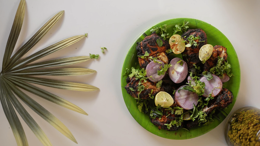 Overhead view of a colourful salad platter topped with sliced red onions and herbs, set beside a tropical palm leaf.